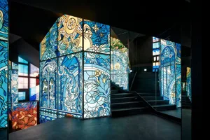 An elegant staircase with a glass railing and metal stairs, surrounded by intricately designed windows in a modern space