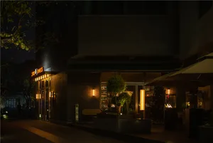 A warm and inviting restaurant at night with a brick exterior, a large tree, and potted plants