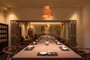 A dining area with a long wooden table set with plates, bowls, cups, and utensils, surrounded by comfortable chairs in an elegant and inviting atmosphere