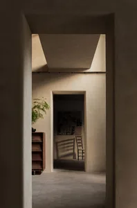 A calm and inviting interior hallway with a doorway, two chairs, and a potted plant, connecting different areas within the building