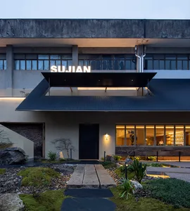 A modern building exterior at night with a black roof, multiple windows, and a clock mounted on one side, conveying a sense of sophistication and contemporary architecture