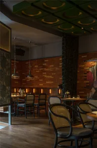 Modern restaurant interior with wooden floor, brick walls, potted plants, and comfortable seating for guests