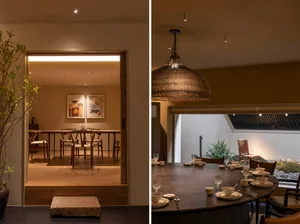 Inviting restaurant space with wooden floors, chairs, tables, and kitchen area with sink and potted plants, well-lit and decorated with wine glasses