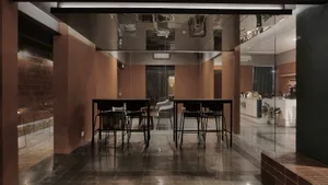 A modern restaurant dining area with three tables and chairs, warm brown and black tones, and well-lit space with natural or artificial light