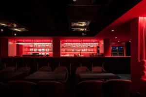 A cozy bar area with a long red counter and chairs, surrounded by bottles and a warm atmosphere