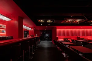 A restaurant interior with red walls and flooring, featuring chairs and tables, a bar with bottles, and a welcoming atmosphere