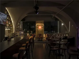 A bar area in a restaurant with wooden chairs and tables, a counter, and bottles of beverages, creating a welcoming atmosphere for socializing