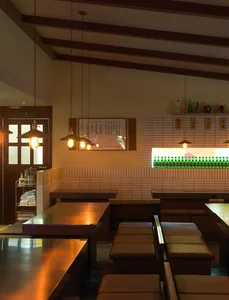 Modern restaurant interior with wooden tables and chairs, bottles on the walls, and a warm atmosphere