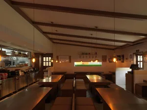 A well-lit restaurant interior with multiple tables and chairs, featuring hanging lights above the tables, creating an inviting and comfortable atmosphere