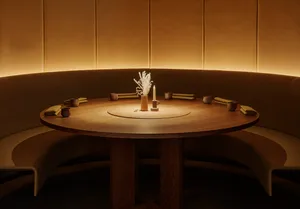 A dining area with a wooden table, chairs, and a vase, set up for a meal or gathering in a warm and inviting restaurant environment