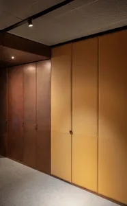 A well-lit hallway with two doors, one brown and one yellow, and a tan wall in between, adorned with warm brown and tan tones