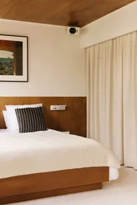 A modern bedroom with a large white bed featuring a black pillow on a wooden headboard, two pictures hanging above, and a bright atmosphere
