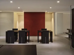 A modern dining area with four black chairs around a wooden table, red accents on the walls, and well-lit space with possible natural or artificial light