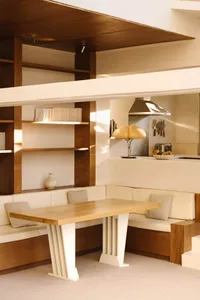 A cozy living space with a wooden dining table, surrounded by chairs, books, and decorative bowls, set in a warm and inviting atmosphere