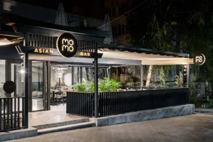 A modern Asian restaurant with a black and white design, featuring tables, chairs, and potted plants, creating an inviting and comfortable atmosphere