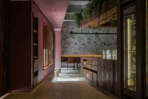 Modern dining space with a pink accent wall, wooden floor, and potted plants, featuring a counter area with chairs
