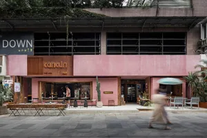 Outdoor cafe with pink building, chairs, tables, umbrellas, and people