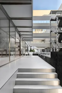 A modern indoor space with multiple levels, white walls, and a mix of chairs, stairs, and an umbrella, creating a well-lit and comfortable atmosphere