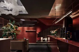 A modern lobby with red walls, wooden floors, and two large vases, well-lit and warm, with stairs in the middle of the room