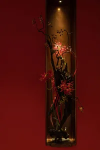 A red wall serves as a backdrop to a colorful floral arrangement in a vase, adding visual appeal to the space