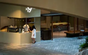 A casual dining space with a counter and seating area, featuring a woman standing behind the counter and chairs and a dining table in the background