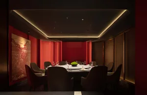 A luxurious dining area with a round table, wine glasses, plates, and cutlery, surrounded by multiple chairs in a warm and cozy red-themed space