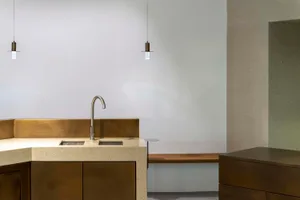 Modern kitchen with marble countertops, a gold faucet, and a dining table, featuring a bench and two sinks