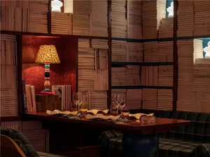 Cozy dining space with a wooden table, chairs, wine glasses, books, and a bookshelf, creating a warm and intellectual atmosphere