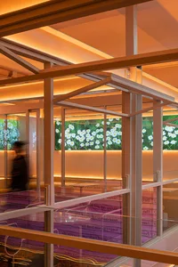 A modern living space with a glass wall, flower display, and natural light, featuring a potted plant and two people