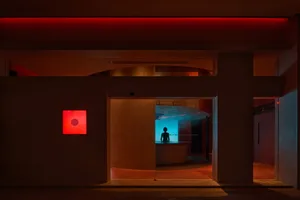 A calm and inviting museum hallway with a red accent wall, neutral tones, and two people walking towards each other