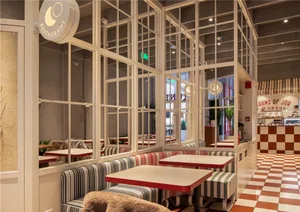 A well-lit restaurant with multiple dining tables, chairs, and large windows allowing natural light to enter the space