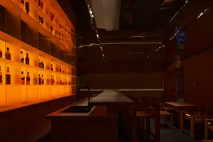 Cozy restaurant with wooden accents, a kitchen counter, and dining tables, featuring bottles and a warm atmosphere