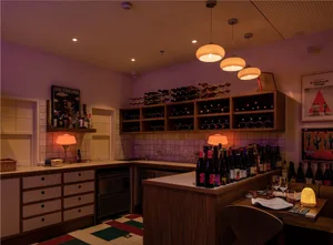 A kitchen with a dining table, wine bottles, and cups, creating a cozy and inviting atmosphere for food and drink preparation