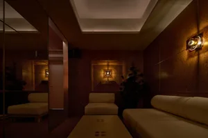 A well-lit living area with a large couch and two chairs in front of a mirror, creating a comfortable atmosphere for relaxation and socializing