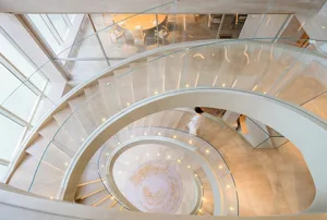 A modern spiral staircase with marble steps, surrounded by a well-lit stairwell, creating a warm and inviting atmosphere