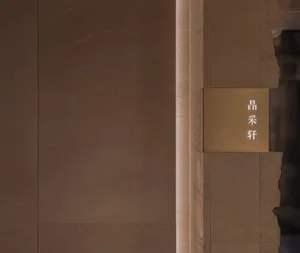 A modern building lobby with an elevator situated between two walls, one of which is a marble wall, and a gold sign above the elevator