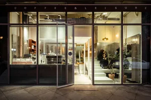 A coffee shop with a glass door entrance, comfortable seating, and potted plants, creating a welcoming atmosphere for socializing and enjoying coffee