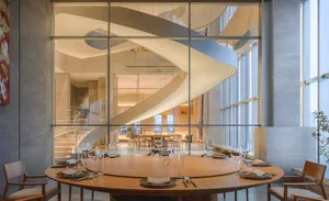 Sophisticated restaurant interior with a wooden spiral staircase, metal railing, and multiple tables and chairs