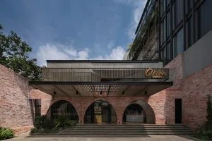 現代建築外觀，磚牆立面、醒目拱門與盆栽植物，左下角有兩個瓶子