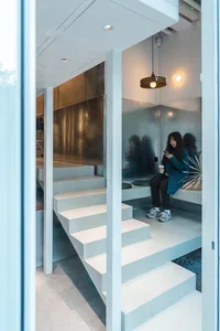 A modern home interior with a staircase, a bench, and two people using their cell phones in a well-lit space