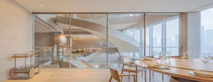 Open living area with a glass spiral staircase, dining table, and multiple couches, giving off a contemporary vibe with clean lines and minimalistic decoration