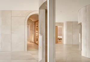 Open concept living area with marble walls, a large archway, and a dining table, with and without wine bottles on the countertop
