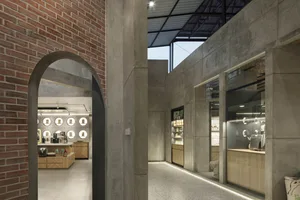 Open modern kitchen and dining area with a large brick wall, various kitchen appliances, and multiple chairs, with scattered bottles and a contemporary feel