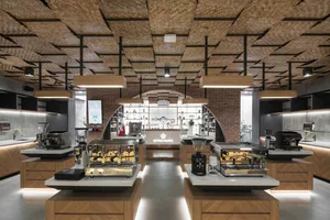 A well-lit coffee shop interior with wooden floors and walls, featuring tables, chairs, and various coffee equipment and supplies on display