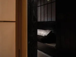 A classic room with a black and white color scheme, featuring a wooden doorway and a large rock on a wooden stand, set against a neutral background
