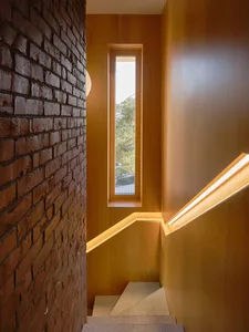 A staircase with a wooden structure and a brick wall with a window, providing natural light into the space below