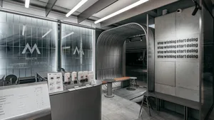 A modern interior design showroom with white and grey walls, featuring two dining tables, a bench, and a chair, with multiple lights enhancing the ambiance