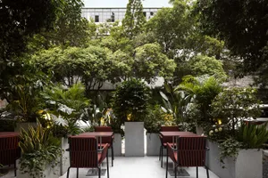 A stone walkway leads to two red chairs and two dining tables in a relaxing outdoor patio setting