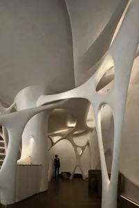 A modern art gallery with curved white walls and ceilings, featuring two people observing exhibits in a dimly lit space