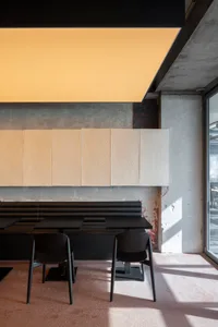 A modern cafe with a concrete wall, large windows, and a cozy atmosphere with three black chairs around a dining table